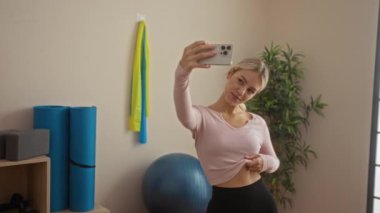 Spor salonunda, sağlıklı yaşam tarzını gösteren spor aletleriyle selfie çeken bir kadın.