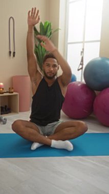 Spor salonundaki yoga minderinin üzerinde gerinen genç bir adam. Arka planda spor aletleri var.