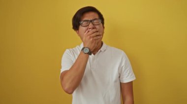 Sarı arka planda esneyen ve gerinen genç bir adam, gözlüklü ve beyaz polo tişörtlü, sabah yorgunluğunu ifade eden ifadeler ve jestler sergiliyor..