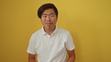 Beyaz gömlekli yakışıklı genç Asyalı canlı sarı bir arkaplan karşısında duruyor, gözlüklü ve elleriyle el kol hareketi yaparak güvenle gülümsüyor..