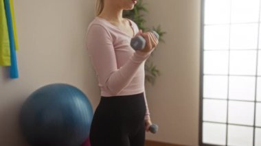 Parlak bir spor salonunda halterlerle egzersiz yapan bir kadın spor topu ve spor bantları takıyor..