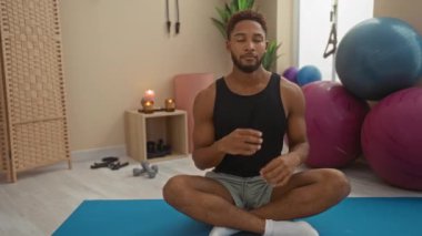 Adam, arka planda mumlar ve ekipmanlarla spor salonundaki yoga minderinde meditasyon yapıyor.