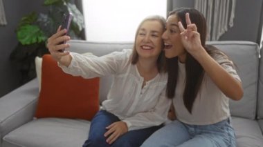 Kanepede telefonla selfie çeken ve oturma odasında eğlenen bir kadın ve kız.