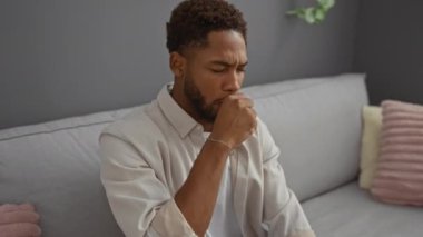 Modern bir oturma odasındaki kanepede oturan genç adam ciddi bir ifadeyle öksürüyor.