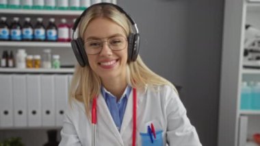 Klinikte kulaklık takan bir kadın gülümseyerek karşılama jesti sergiliyor. Etrafı tıbbi malzemelerle çevrili ve profesyonel sağlık hizmetlerini sembolize eden dosyalar hazırlıyor..