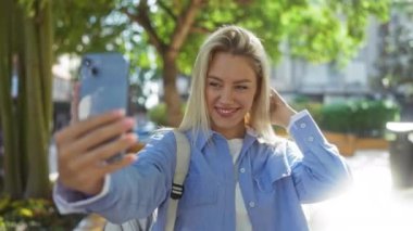Güneşli şehir parkı ortamında selfie çekerken gülümseyen kadın, gençlik keyfi ve doğa geçmişiyle bağlantı kurmanın özünü yakalıyor, günlük giysiler giyiyor..