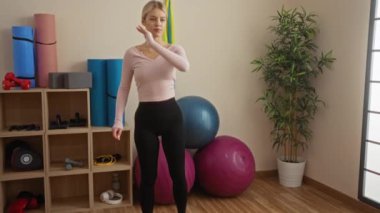 Spor salonunda spor aletleriyle egzersiz yapan bir kadın, egzersiz topları ve yoga minderleriyle çevrili modern bir iç mekanda sağlıklı bir yaşam tarzı sergiliyor..