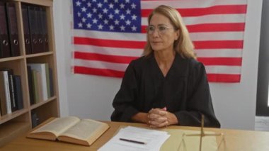 Mahkeme salonunda arka planda Amerikan bayrağı olan yargıç cübbesi giyen bir kadın, yasal belgelere ve masanın üzerindeki hukuk kitabına odaklanıyor..