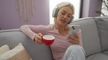 Kanepede kulaklıklarla dinlenen, kırmızı bardaktan içen, akıllı telefon kullanan, rahat oturma odasında, müzikten hoşlanan, günlük giysiler, doğal ışıklandırma....