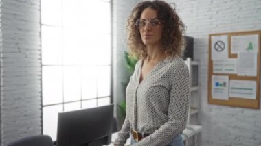 Modern ofis ortamında kendine güvenen bir kadın, kollarını kavuşturmuş, parlak doğal ışıkla çevrili, profesyonel ve şık bir görünüm sergiliyor..