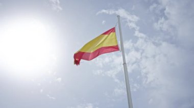 İspanyol bayrağı parlak bir güneşe ve açık gökyüzüne karşı sallanıyor vatansever bir ortamda gün ışığında bir bayrak direğinde..