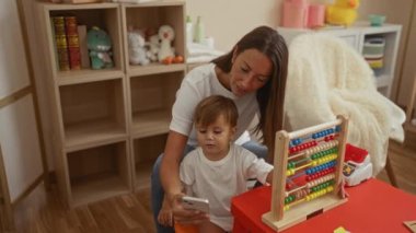 Kadın ve çocuk telefonda oyuncaklarla ve abaküsle gülümsüyor. Bu da evde sevgi dolu bir anne-oğul bağı ve eğitici bir oyun zamanı olduğunu gösteriyor..