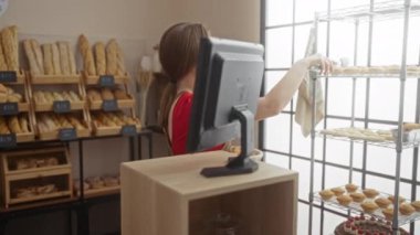 Kapalı bir pastanede çalışan genç bir kadın hamur işleri yapıyor ve modern ekmek dükkanında önlük giyerken gülümsüyor.