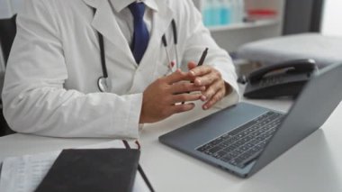 Bir klinikte dizüstü bilgisayarla çalışan bir doktor hasta bilgilerini tartışır, yanında steteskop ve telefon bulunan bir masada beyaz önlük giyerek sağlık hizmetlerini sembolize eder..