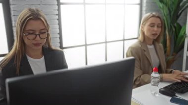Modern bir ofiste birlikte çalışan kadınlar, bilgisayar kullanıyor ve büyük pencereleri ve iş kıyafetleri olan parlak, profesyonel bir çevrede bir projeyi tartışıyorlar..