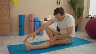 Sağlık odasındaki yoga minderinin üzerinde mumlar ve egzersiz aletleriyle gezen bir adam..