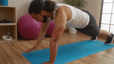 Evde yoga minderinde egzersiz yapan bir adam sağlıklı bir yaşam tarzını geliştiren spor aletleri arasında güç ve zindelik odaklı bir sağlık merkezinde şınav çekiyor..