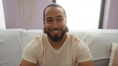 Sıcak bir oturma odasında gülümseyen gözlüklü bir adam gün ışığında evde huzurlu bir ev ortamını yakalıyor..