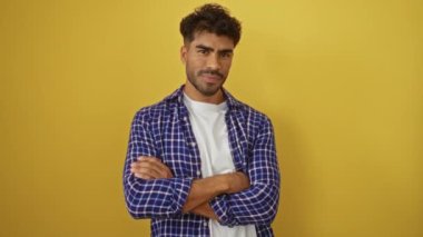 Sakallı genç adam kollarını kareli gömleğiyle parlak sarı bir arkaplan, etkileyici ve modern tarzıyla birleştirdi..