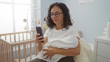 Kadınlar bebek beşiği yaparken rahat bir kreşte akıllı telefon kullanır. Kapalı alanda huzurlu bir an yakalar. Teknoloji ve bakım üzerine odaklanır..