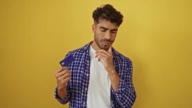 Kredi kartlı genç adam, ekose gömlek giyen parlak sarı duvara karşı düşünceli bir şekilde düşünür..