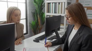 Modern ofis ortamında, bilgisayarlarla, belgelerle ve arka planda parlak bir pencereyle tartışan ve el sıkışan iş kadınları.