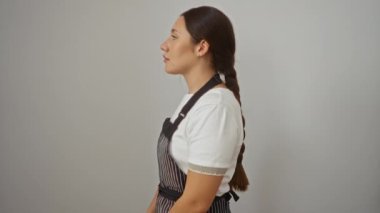 Önlüklü kendine güvenen genç İspanyol kadın profilde doğal bir şekilde poz veriyor, gülümsüyor ve beyaz arka planda izole edilmiş bir şekilde yan tarafa bakıyor.