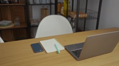 Oturma odasında rahat bir şekilde kahve içerken kağıt okuyan bir kadın. Laptop telefonu ve not defteri ahşap masada.