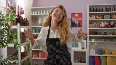 Çizgili önlüklü, sarı saçlı genç bir kadın renkli dekorasyon ve bitkilerle çevrili şık bir ev dekorasyonunda gülümseyip dans ediyor.