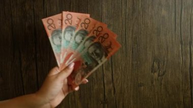 Avustralya 'nın yirmi dolarlık banknotlarını ahşap bir arka planda tutan kadın, birden fazla para birimini gösteriyor.