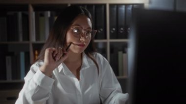 Bir kadının elinde arka planda kitap rafları olan bir kalem tutarak bir ofiste tefekkür etmesi, bir işyeri için profesyonel ve yansıtıcı bir atmosfer yaratması