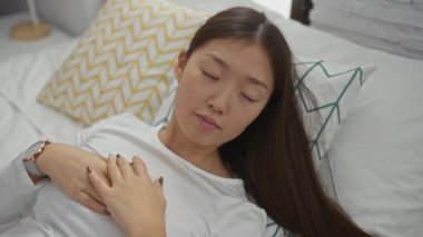 Yatak odasında rahat bir yatakta uzanan, elleri göğsünde beyaz bir gömlek giyen bir kadın evde rahatlama ve huzur öneriyor..