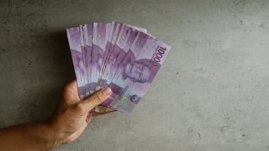 Beton zemine karşı birden fazla Endonezya rupiası banknotunun el ele tutulması, para ve işlemin vurgulanması.