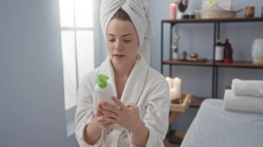 Kaplıcadaki kadın, kapalı bir sağlık merkezinde mumlar ve rahatlatıcı bir ortam varken ürün etiketi okuyor.