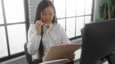 Modern ofisteki belgeleri inceleyen kadın, kapalı alandaki büyük pencerelerin yanında gözlük takıyor.