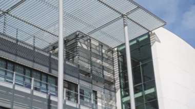 Parlak gökyüzü altında metalik cepheli ve cam pencereli modern mimari yapısal tasarım ve kentsel estetiği ön plana çıkarıyor.