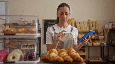 Genç İspanyol esmer kadın bir pastanede çalışıyor. Etrafı pasta ve ekmekle çevriliyken bir tablet kullanıyor.