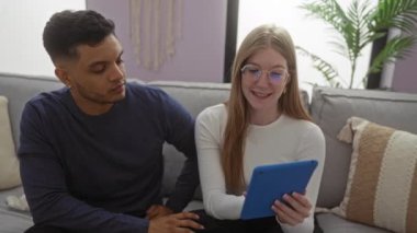 Oturma odasındaki bir çift, evde aşk ve mutluluğu gösteren tablet kullanarak bir anı paylaşıyor. Kanepede romantik bir ilişki yaşıyorlar..