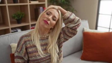 Rahat oturma odasında, rahat koltukta uzanan, sarı saçlı, sıradan bir kazak giyen, evinde huzurlu bir anın tadını çıkaran bir kadın..