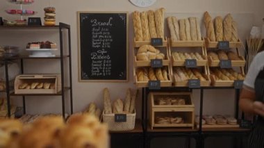 Kapalı bir pastanede duran genç bir kadın arka planda çeşitli ekmek ve hamur işleri sergilenen bir fincan kahve ikram ediyor.