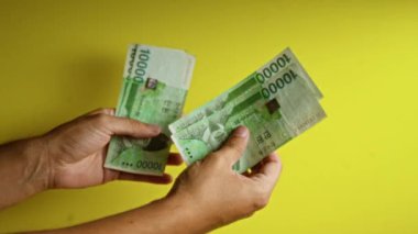 Kore 'yi elinde tutan ve sayan adam, eller, parmaklar, para, para ve finansal kavramlara odaklanan sarı bir arkaplana karşı banknotlar kazandı..