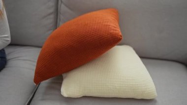 Kadın rahat bir kanepede portakal rengi yastıkla rahat bir oturma odasında dinleniyor, günlük giysiler giyiyor, gün içinde sakin ve rahat görünüyor..