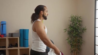 Sağlık merkezindeki sakallı adam, spor kıyafetleri ve bitkilerle çevrili boynu beyaz havluyu perdelerek kapalı bir kaplıca ortamı yaratıyor..