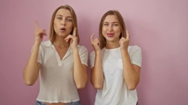 Pembe bir duvara karşı komik ifadeler sergileyen kız kardeşler neşeli hareketler ve gülücüklerle aile sevgisini ve bağlantısını gözler önüne seriyorlar..
