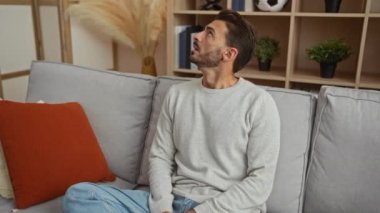 Oturma odasında hayal kırıklığına uğrayan genç adam evdeki gürültü yüzünden kulaklarını yastıkla kapatıyor..