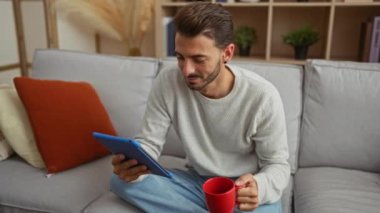 Evde kahve içip tablet kullanan genç adam evdeki parlak oturma odasında rahat bir dekorla oturuyordu.