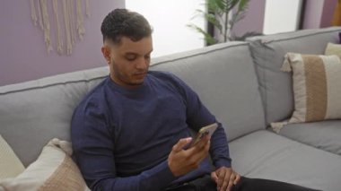 Erkek, akıllı telefonuyla kanepede dinlenirken kadın şakacı bir şekilde onu kavrayıp oturma odasında sarılıyor..