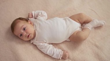 Bebek çocuk yatak odasında uzanıyor, sevimli ve sevimli yüz hatları sergiliyor rahat bir ev ortamında, çocukluk masumiyetini somutlaştırıyor..