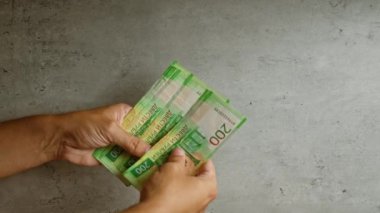 Kabataslak beton bir zemine karşı Rus rublesini tutan ve sayan eller 200 rublelik banknotları gösteriyor..