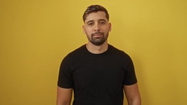 Parlak sarı bir arkaplan önünde gülümseyen genç adam pozitif ruh hali ve gündelik tarzını sergiliyor..